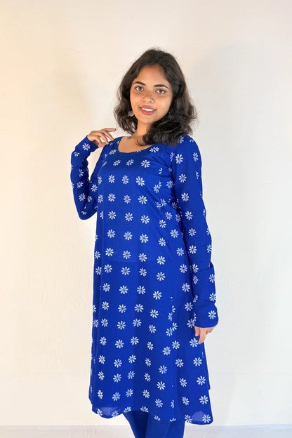 Woman wearing a blue dress with white floral patterns against a plain background