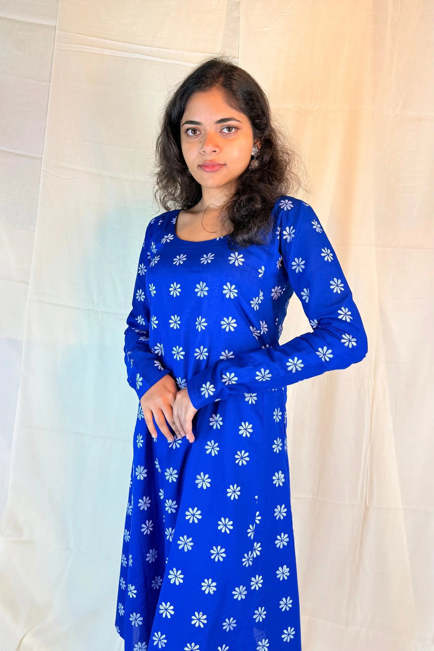 Woman wearing a blue dress with white floral patterns against a white curtain background