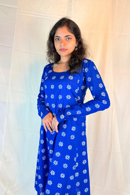 Woman wearing a blue dress with white floral patterns against a white curtain background