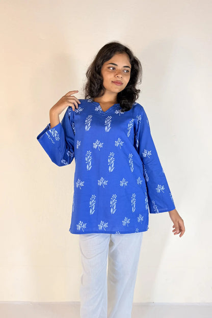Woman wearing a blue patterned top and light pants against a plain background