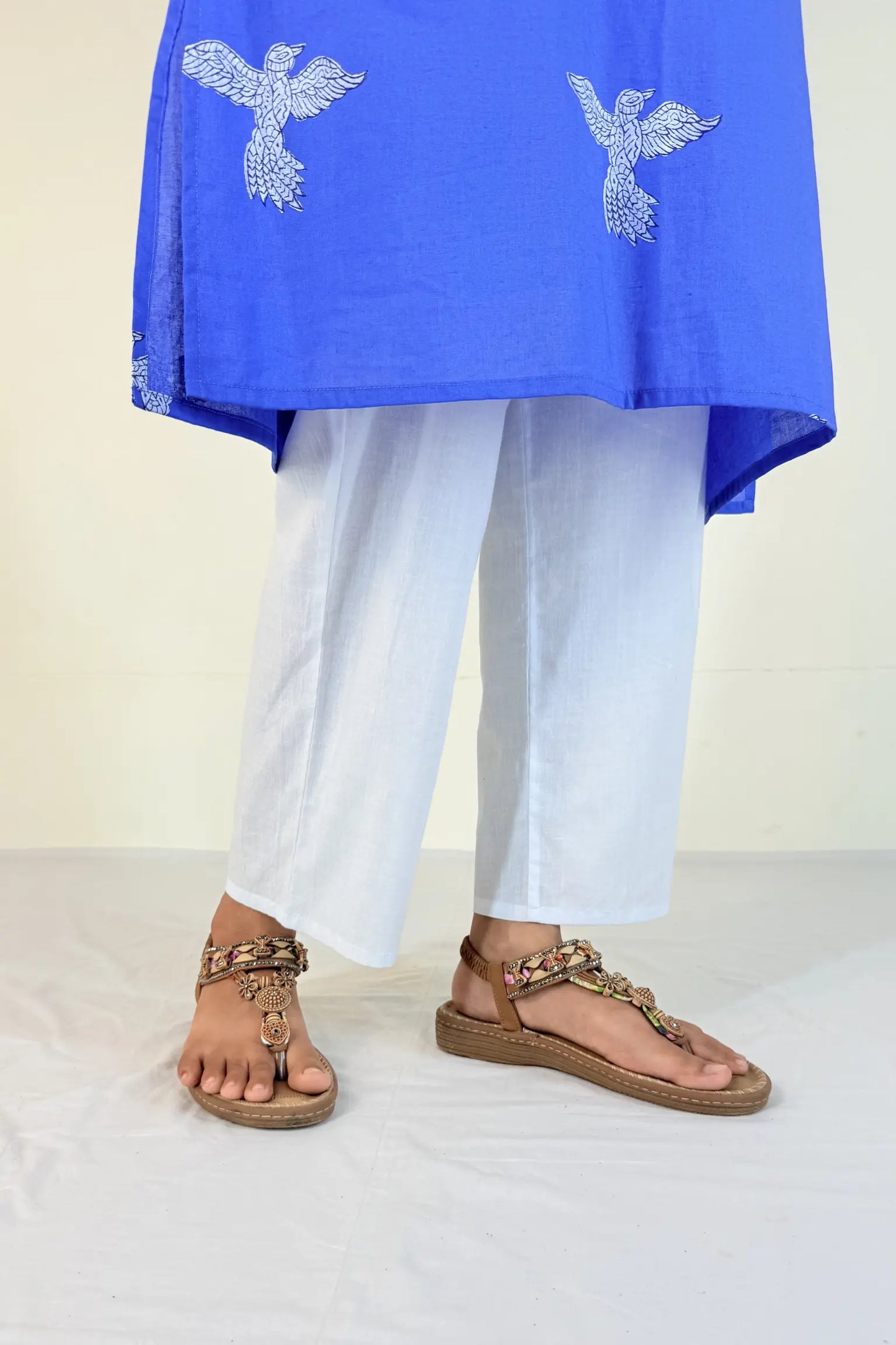 Person wearing a blue top with white embroidery and white pants, standing on a light background