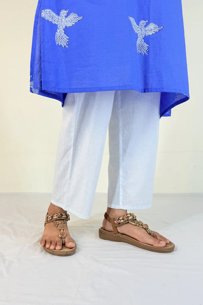 Person wearing a blue top with white embroidery and white pants, standing on a light background