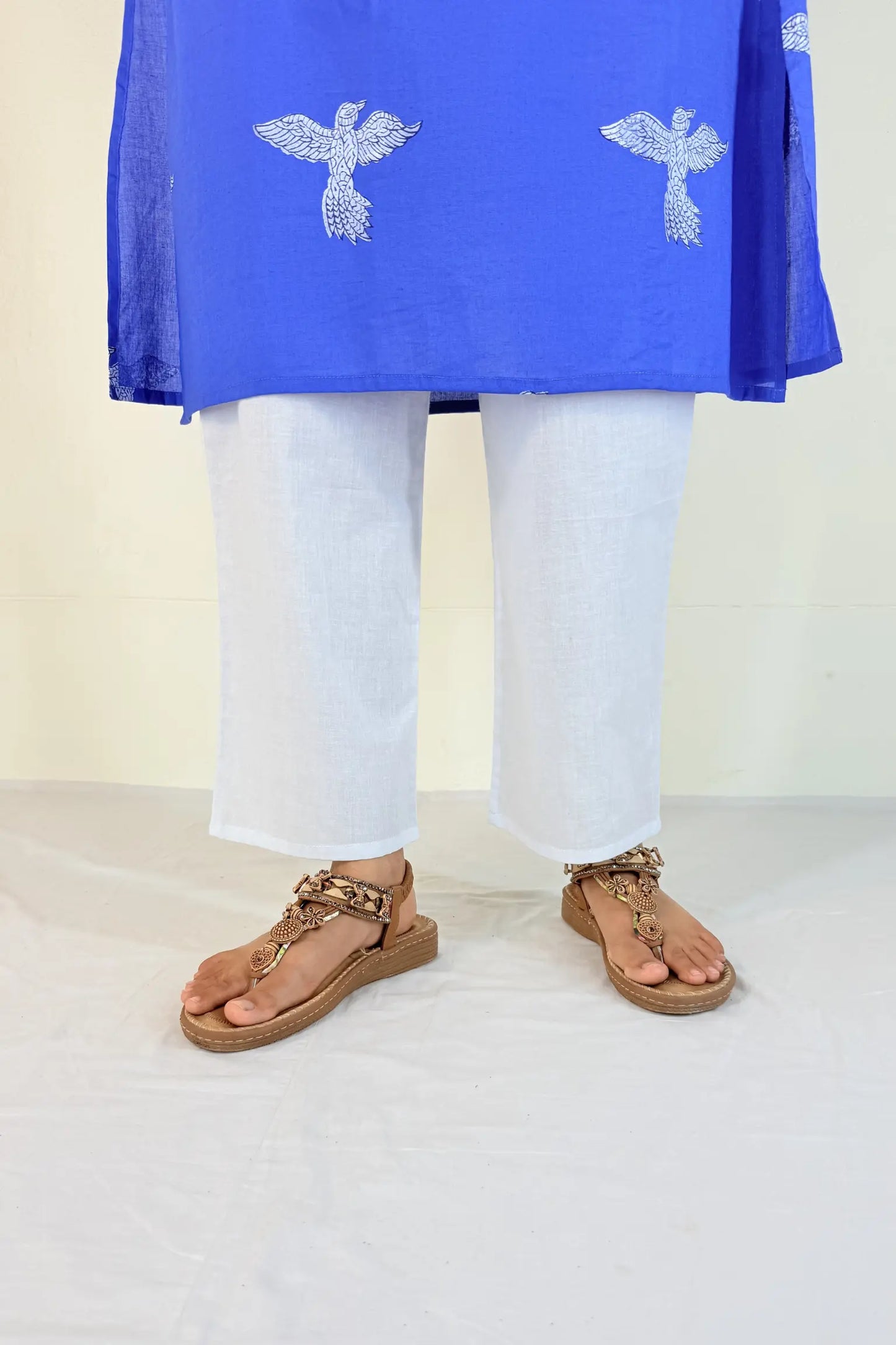 Person wearing a blue top with white patterns and white pants on a plain background