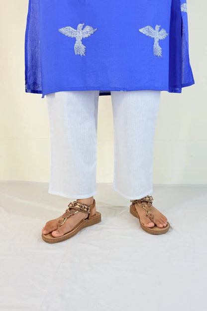 Person wearing a blue top with white patterns and white pants on a plain background