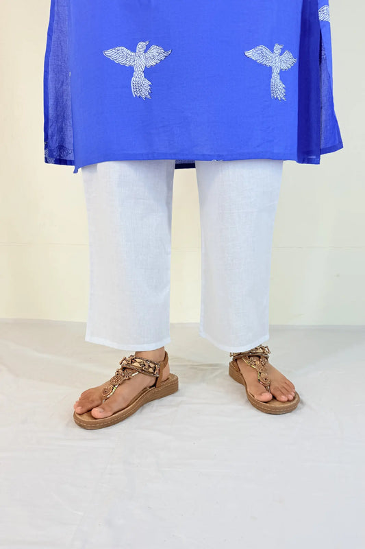 Person wearing a blue top with white patterns and white pants on a plain background
