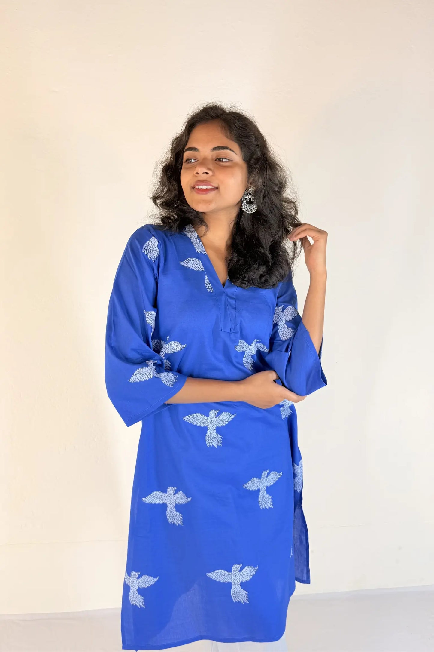 Woman wearing a blue dress with white patterns against a plain background