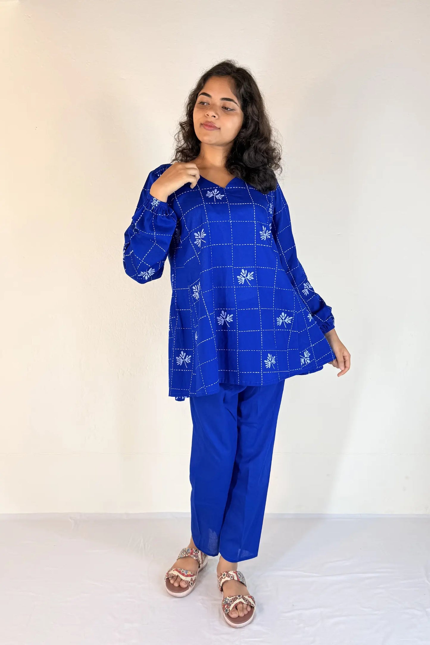 Woman wearing a blue traditional outfit with white patterns on a plain background