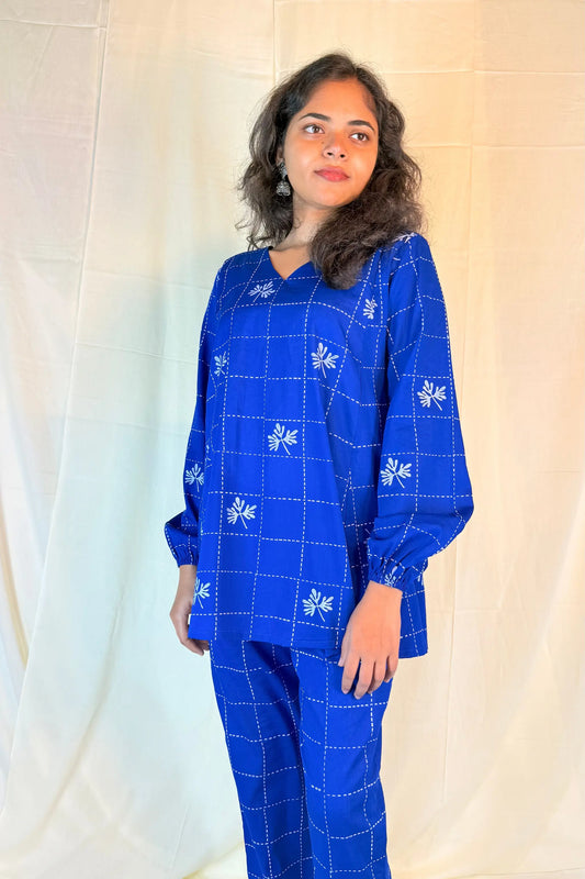 Woman wearing a blue embroidered outfit against a plain background