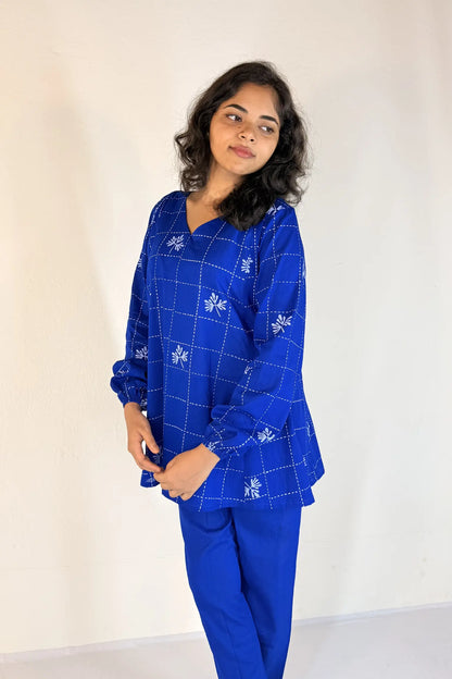 Woman wearing a blue outfit with white patterns against a plain background