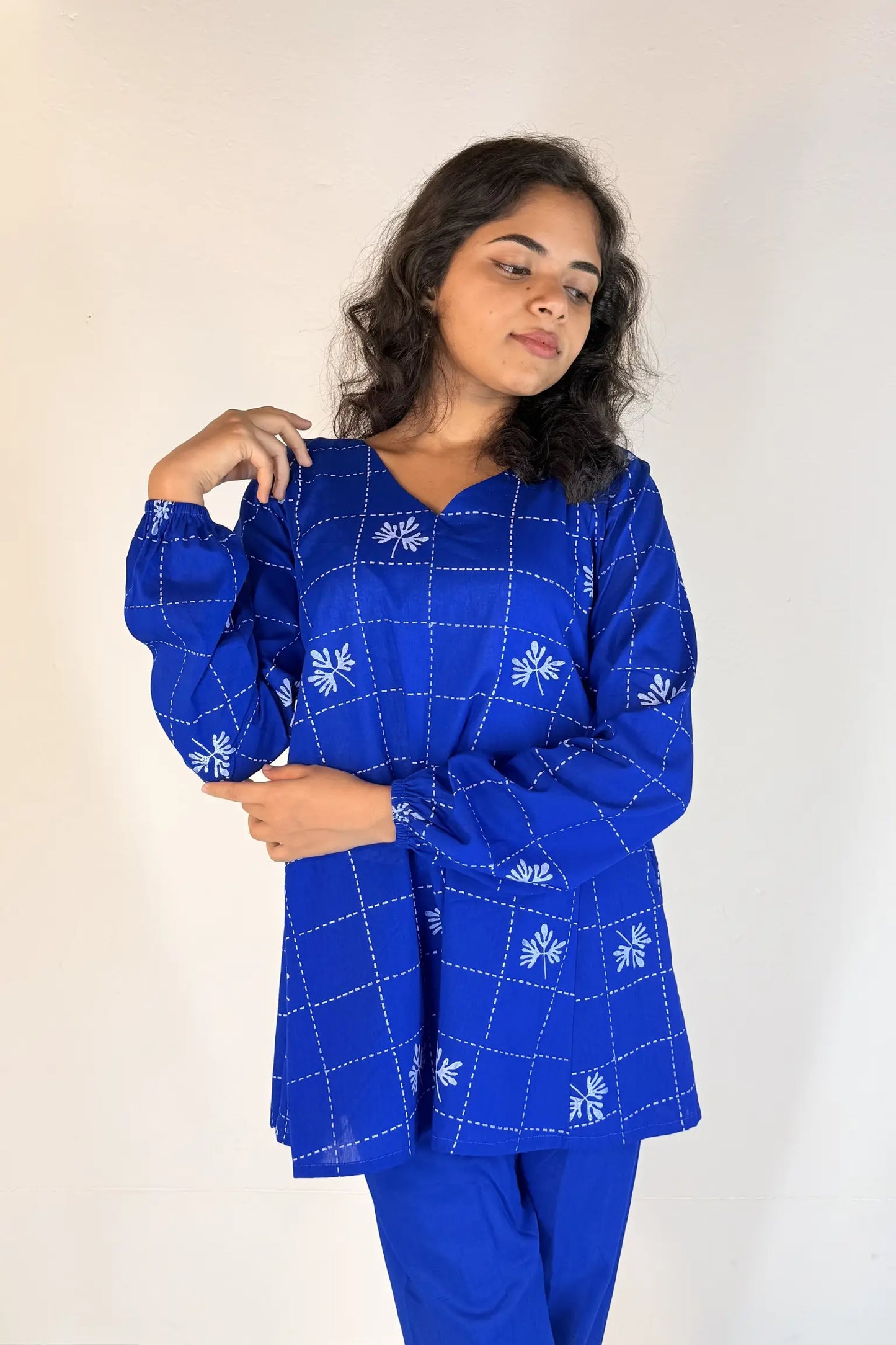 Woman wearing a blue traditional outfit with white patterns on a plain background