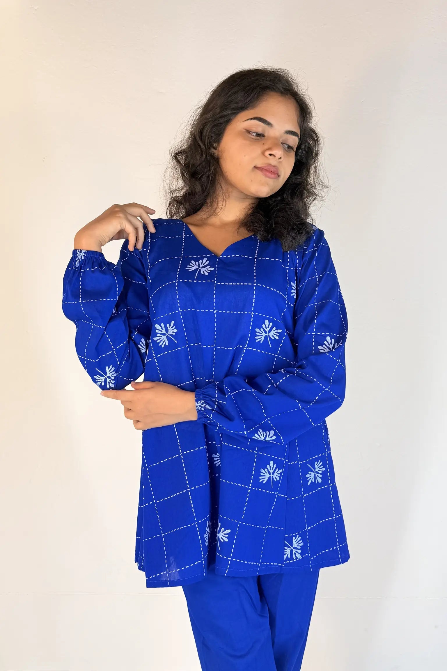 Woman wearing a blue traditional outfit with white patterns on a plain background