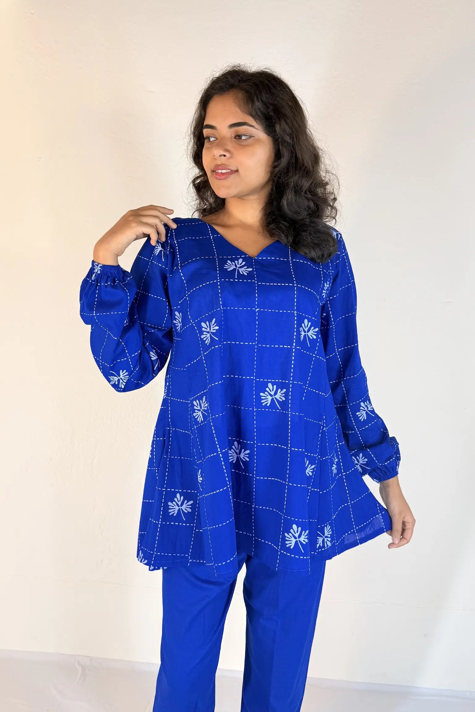 Woman wearing a blue outfit with white patterns against a plain background