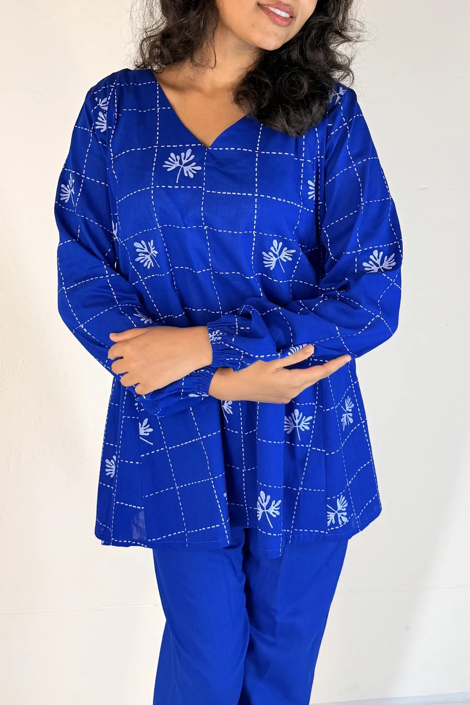 Woman wearing a blue outfit with white patterns against a plain background