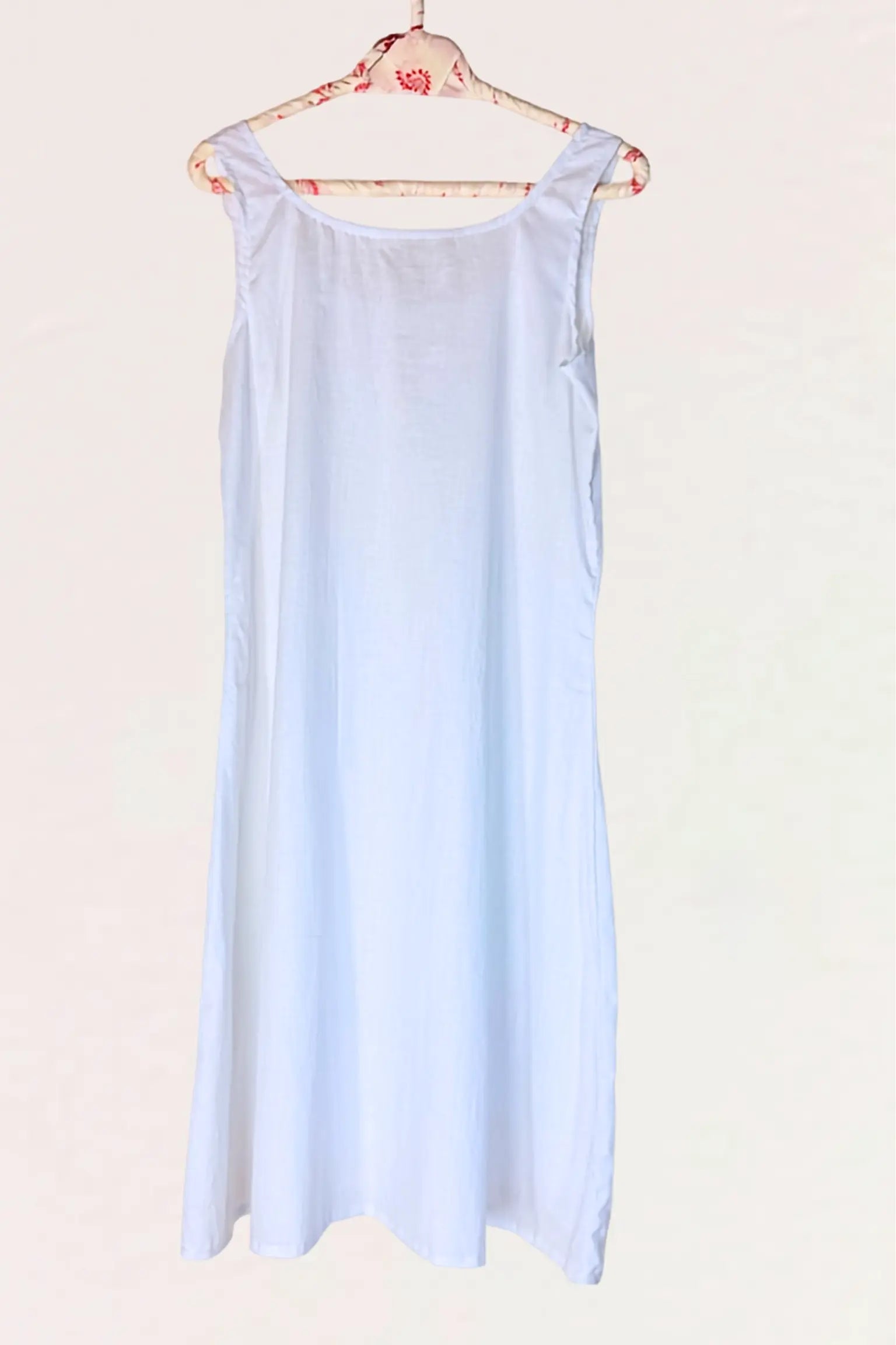 A light blue sleeveless slip dress hanging on a floral-patterned wooden hanger against a plain off-white background.