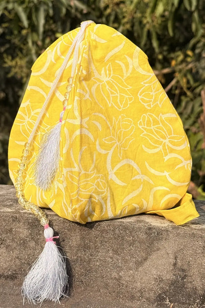 Yellow fabric pouch with floral patterns and tassels on a stone surface with green foliage in the background