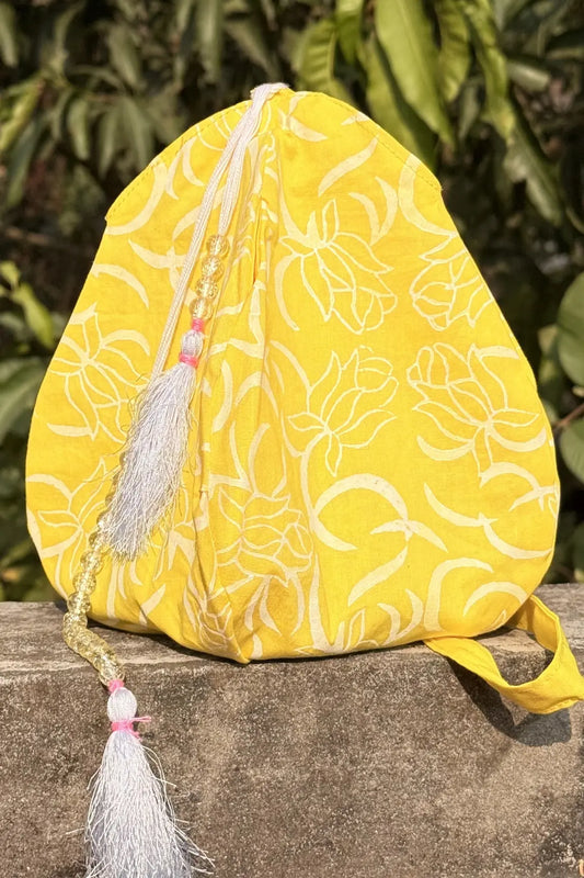 Yellow fabric pouch with floral patterns and tassels on a stone surface with green foliage in the background