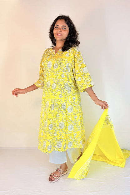 Woman wearing a bright yellow embroidered kurta with white pants on a light background
