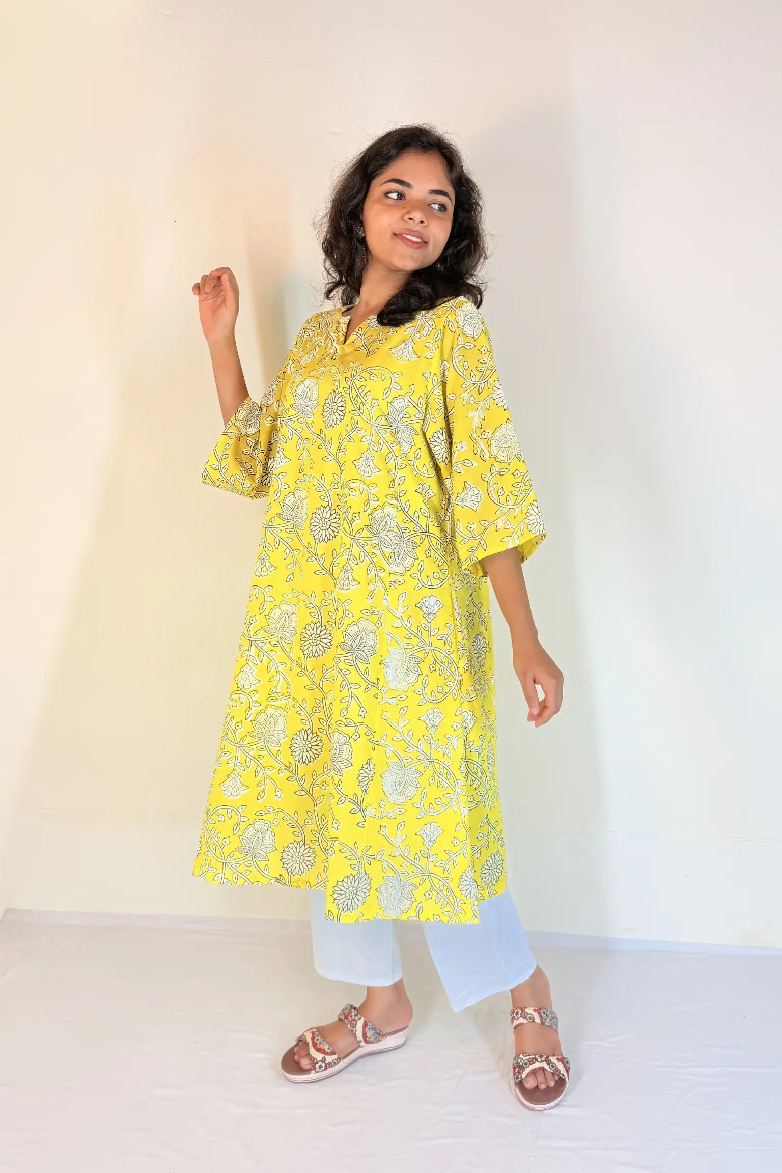 Woman wearing a yellow floral kurta with white pants against a plain background