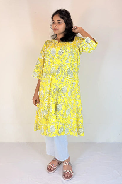 Person wearing a yellow floral kurta with white pants on a plain background