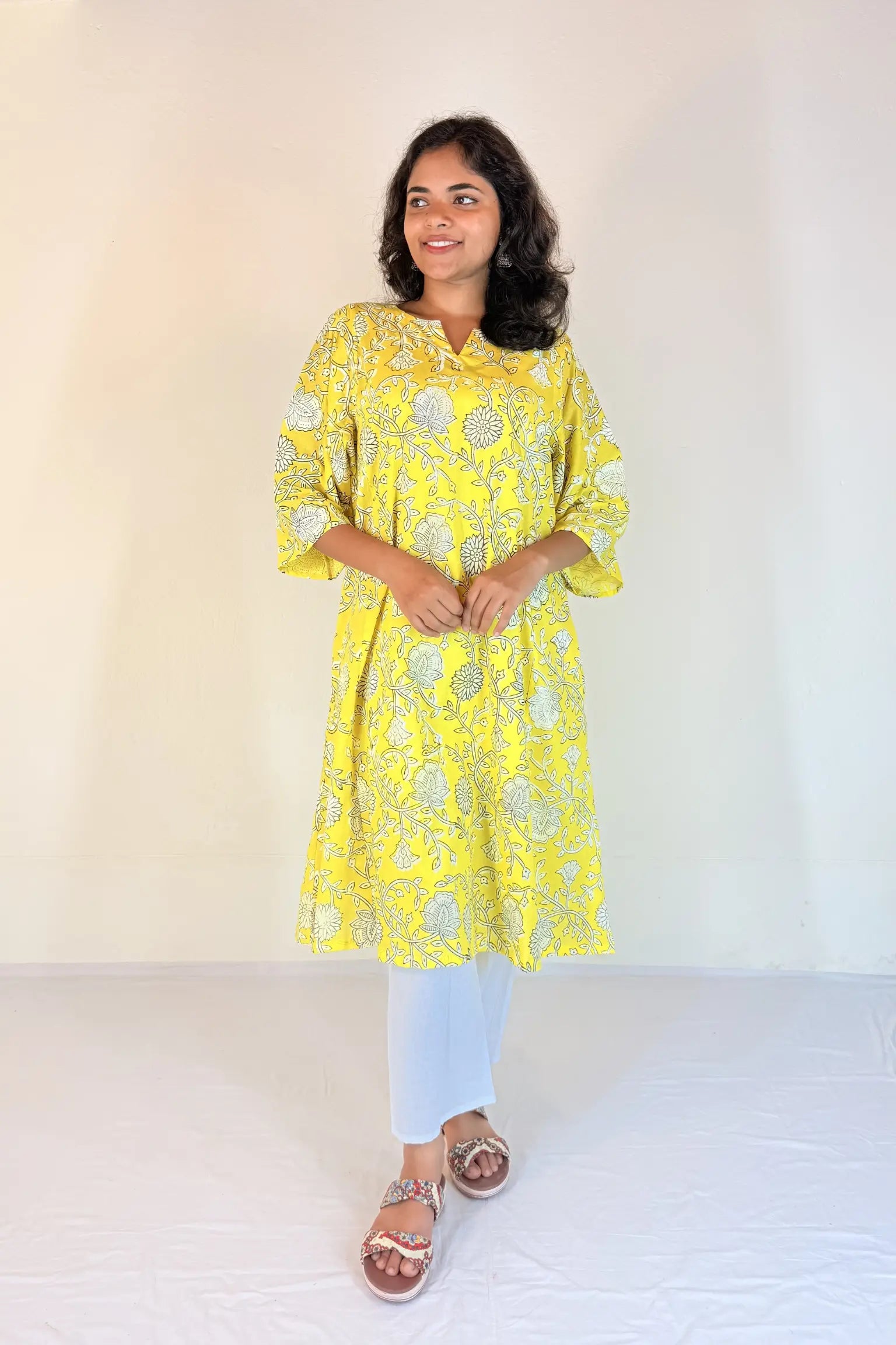 Woman wearing a yellow floral kurta with white pants against a plain background