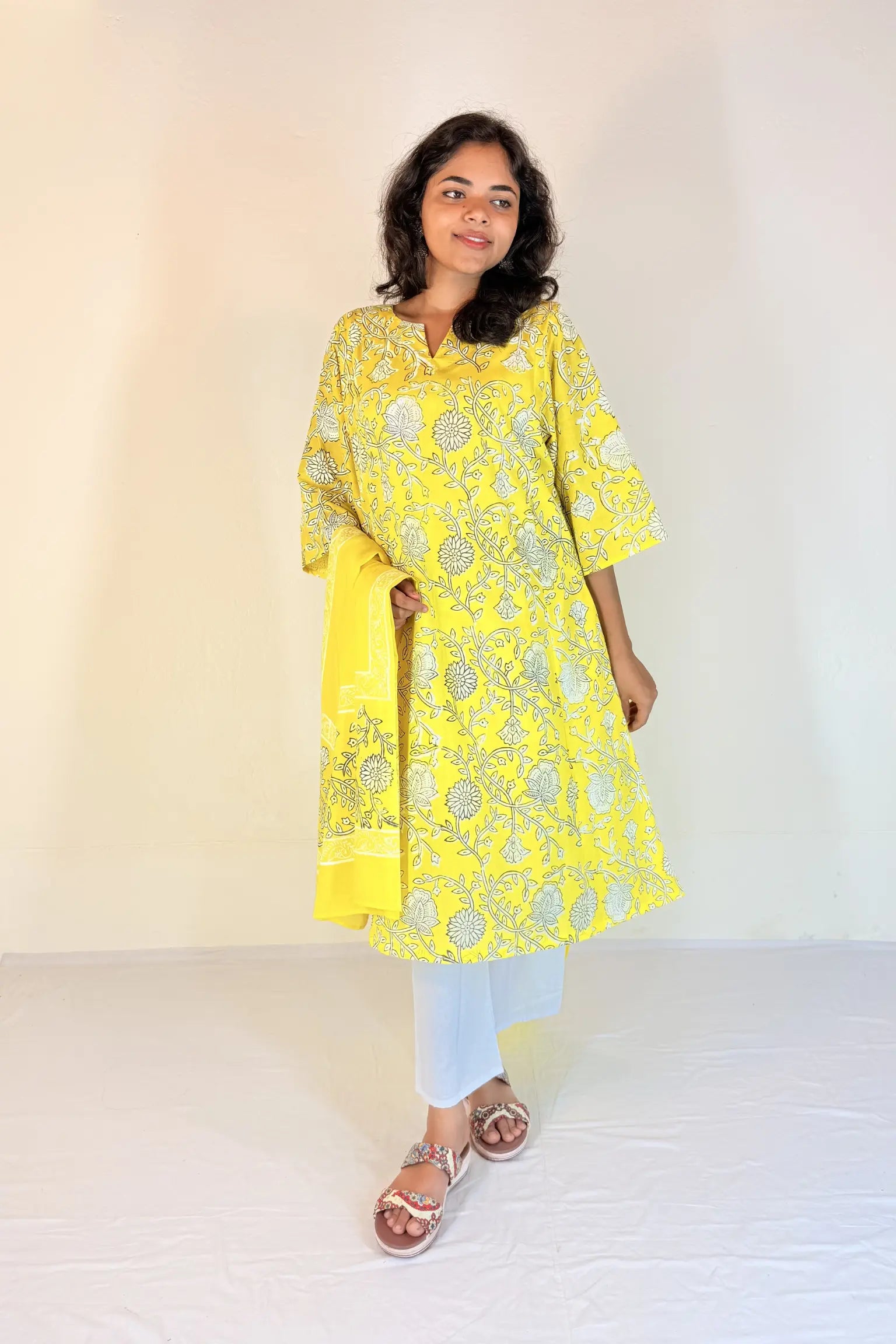 Woman wearing a yellow embroidered kurta with white pants on a plain background