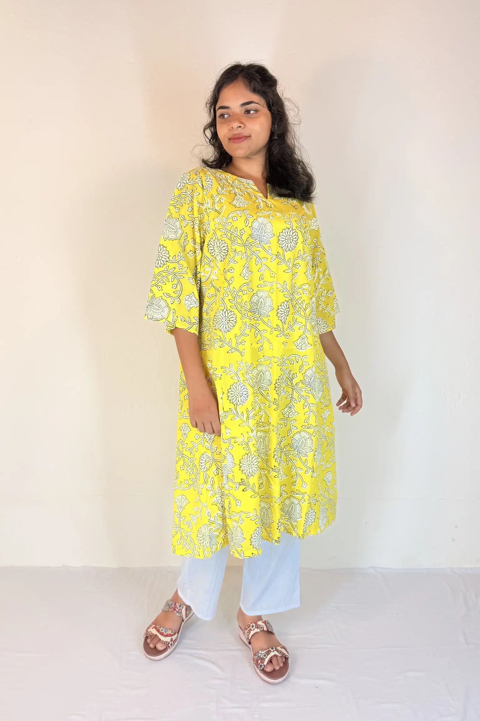 Woman wearing a yellow floral kurta with white pants against a plain background