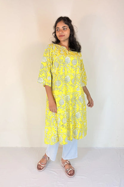 Woman wearing a yellow floral kurta with white pants against a plain background