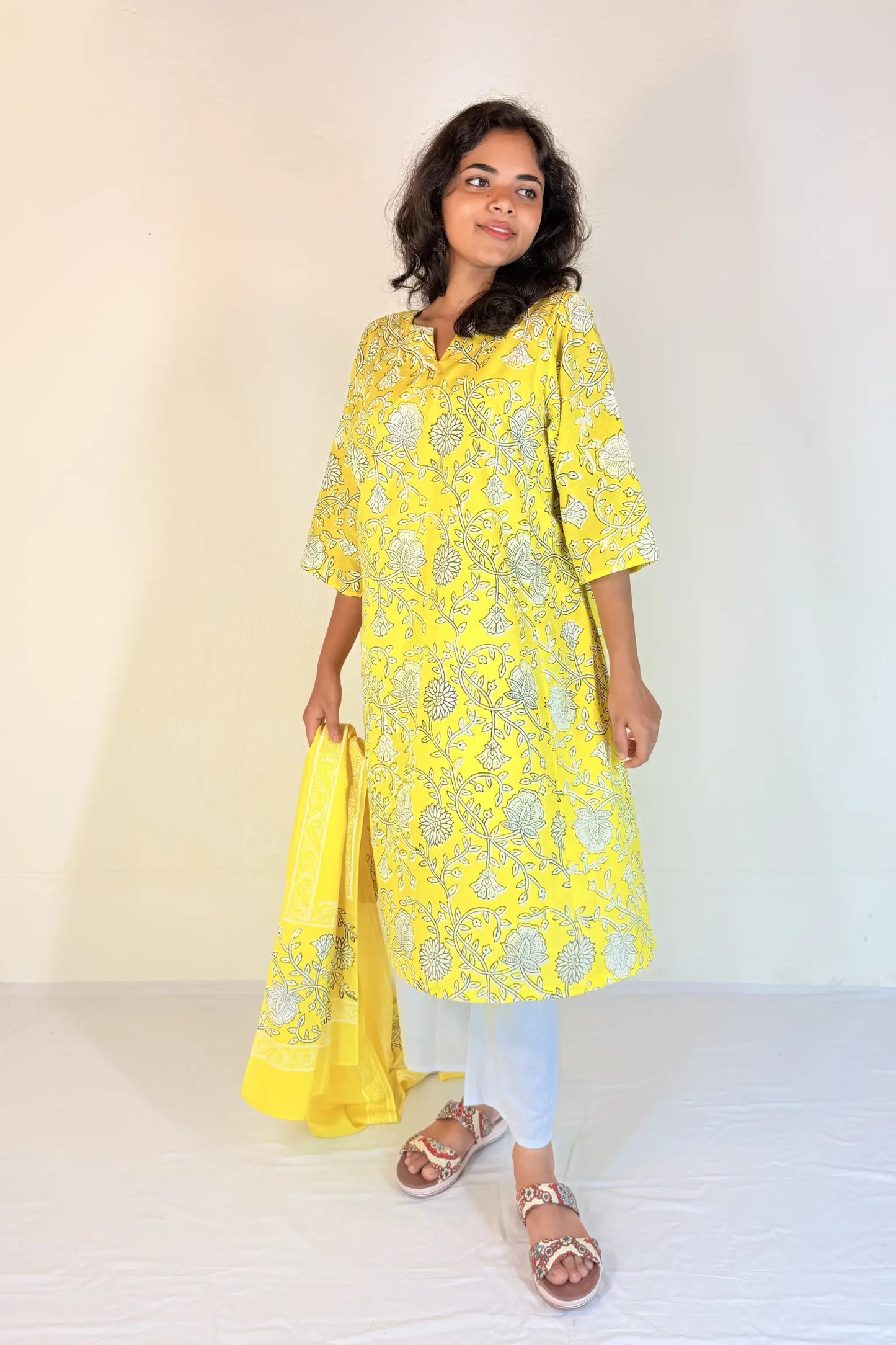 Woman wearing a yellow embroidered kurta with white pants against a plain background