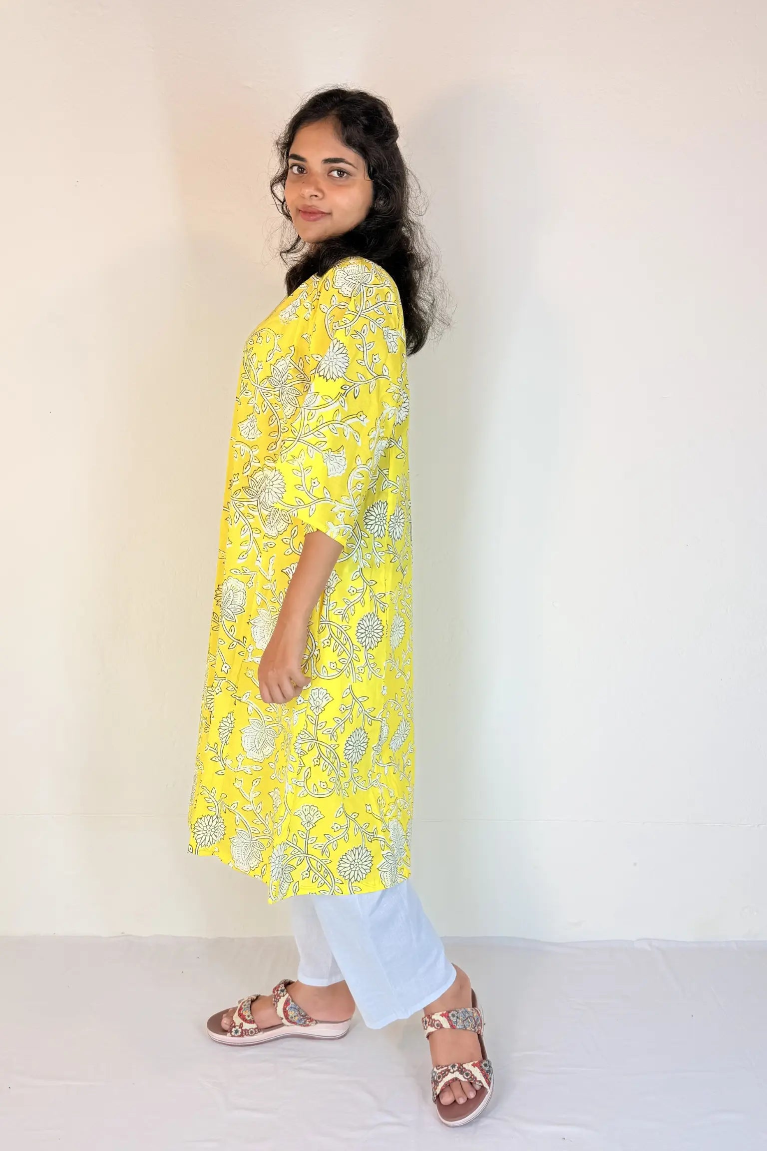 Woman wearing a yellow floral kurta with white pants against a plain background