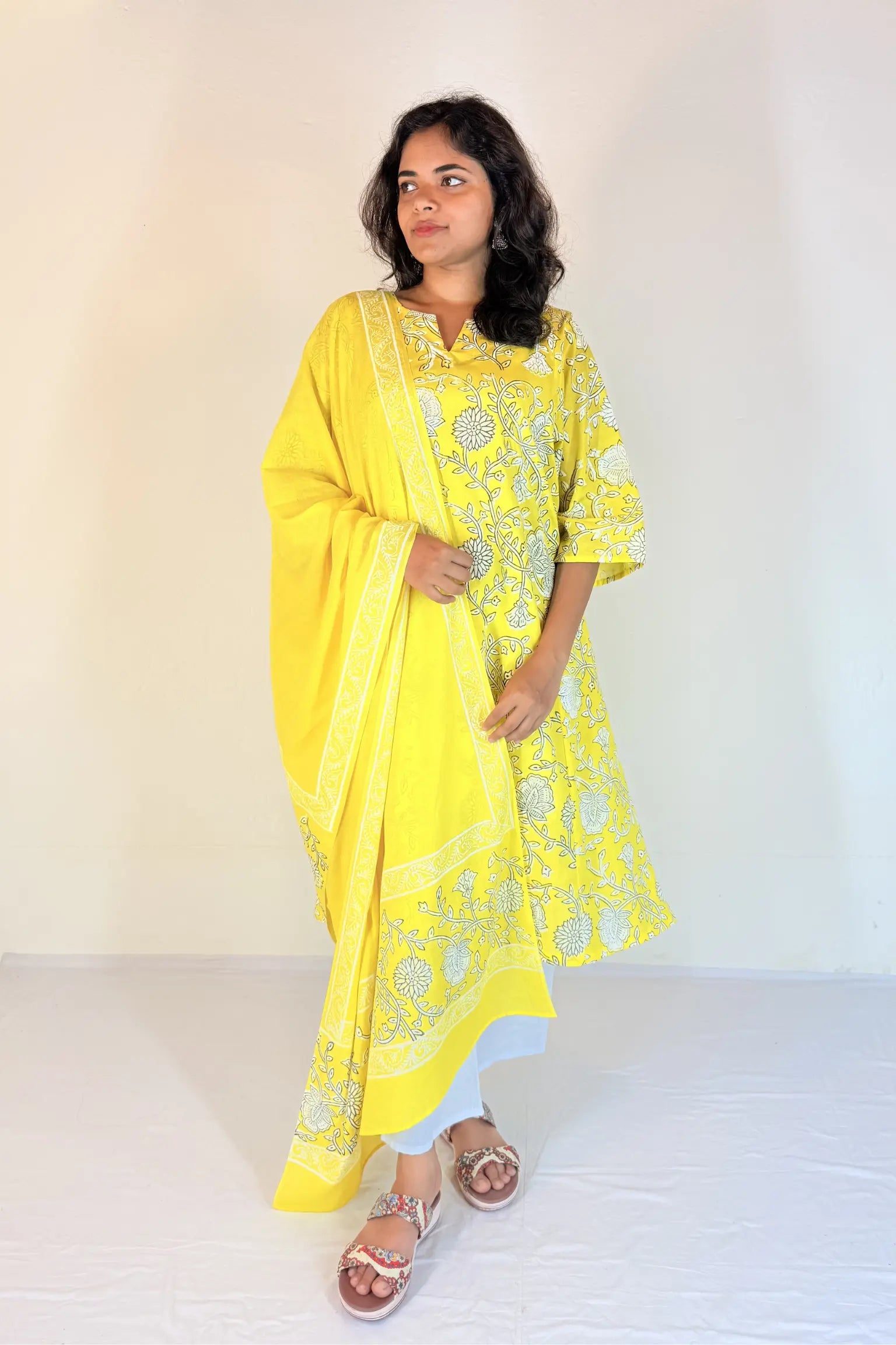 Woman wearing a yellow traditional outfit with white patterns on a plain background