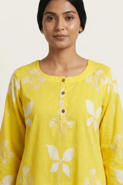 A woman wearing a bright yellow long-sleeve kurta with a white floral block print and a buttoned neckline, shown against a plain light background.