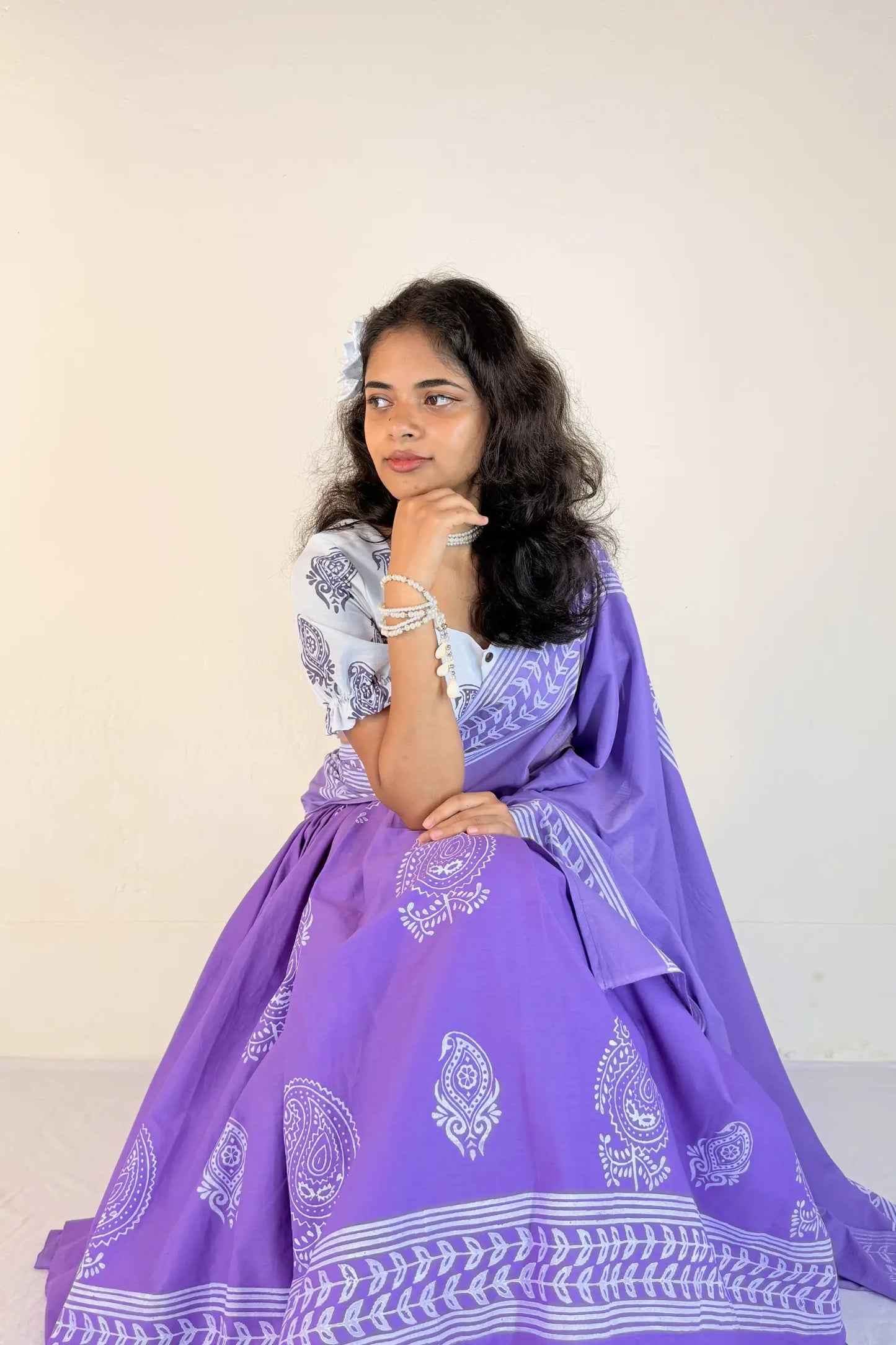 Woman wearing a purple traditional outfit with white patterns on a plain background