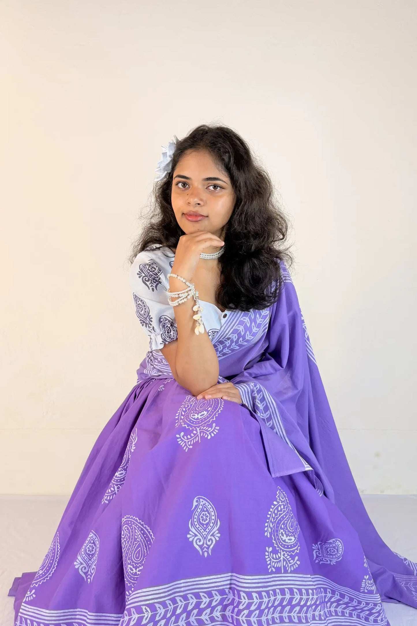 Woman wearing a purple traditional outfit with white patterns on a plain background