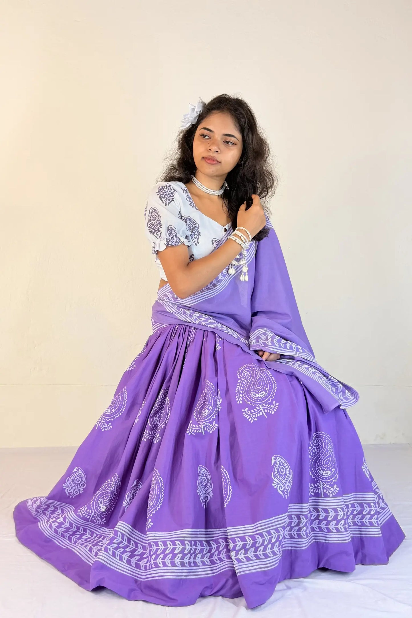 Woman wearing a purple traditional outfit with white patterns on a plain background