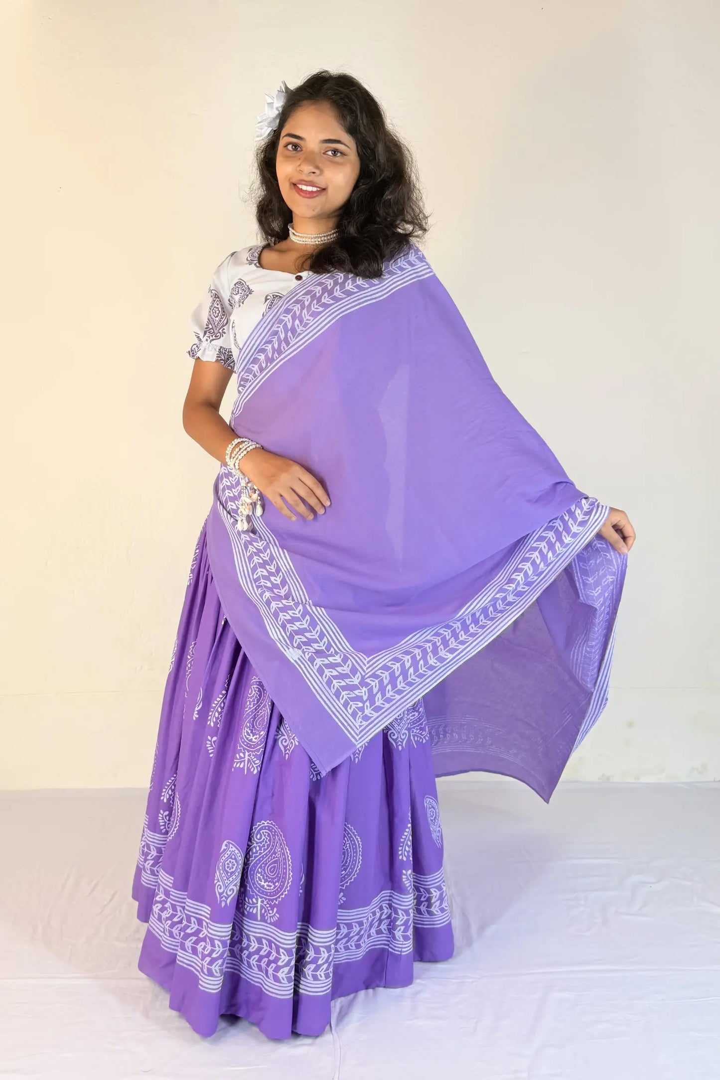 Woman wearing a purple traditional outfit with white patterns on a plain background