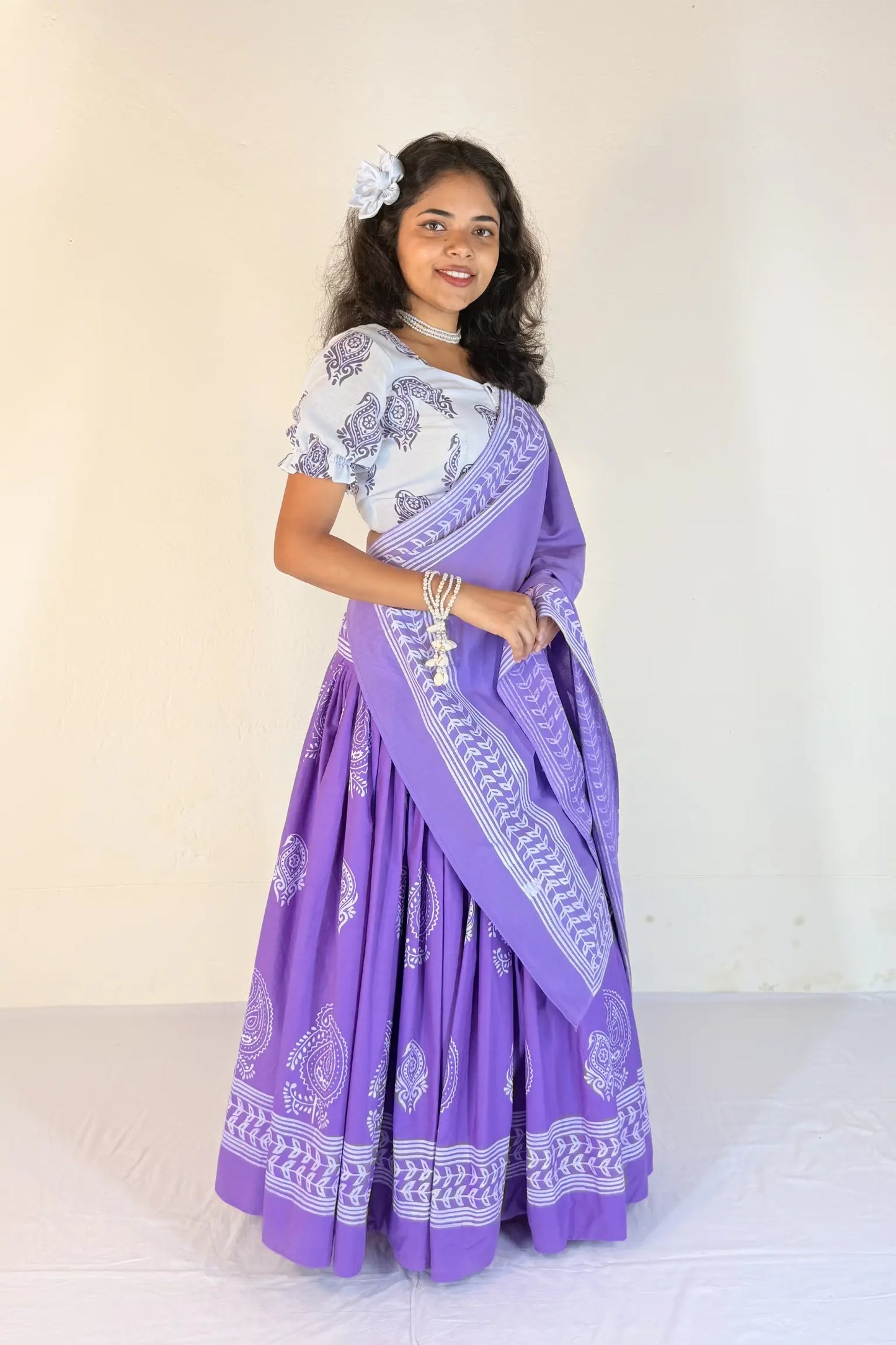 Woman wearing a purple and white traditional outfit with a matching scarf against a plain background