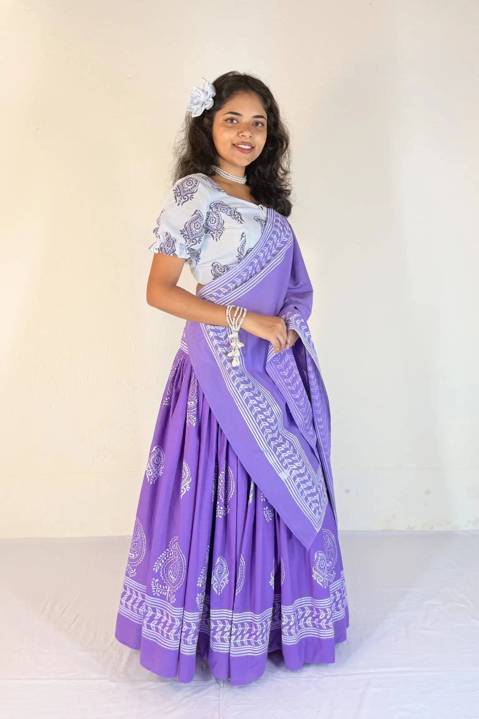 Woman wearing a purple and white traditional outfit with a matching scarf against a plain background
