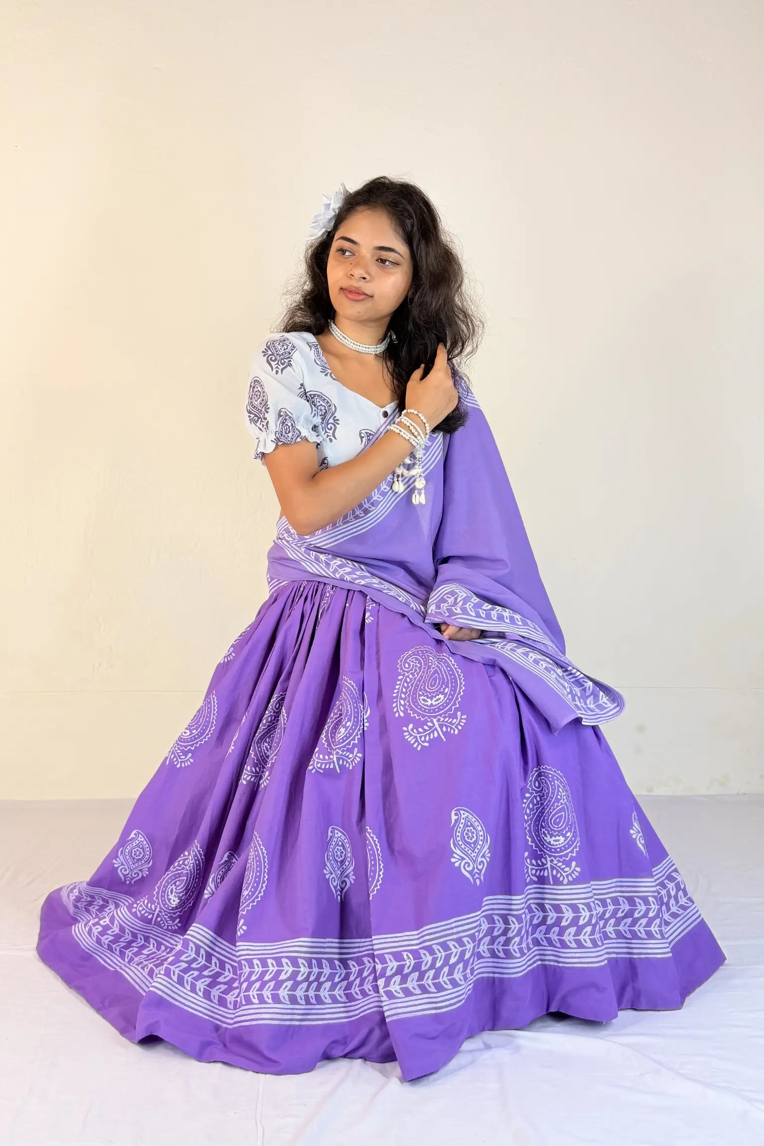 Woman wearing a purple traditional outfit with white patterns on a plain background