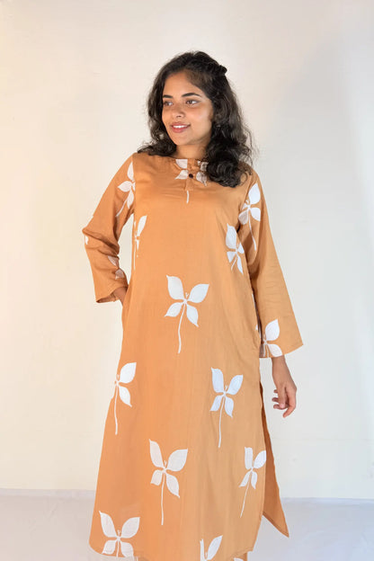 Woman wearing a mustard yellow dress with white floral patterns against a plain background
