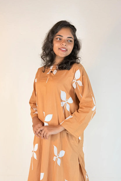 Woman wearing a brown dress with white floral patterns against a plain background