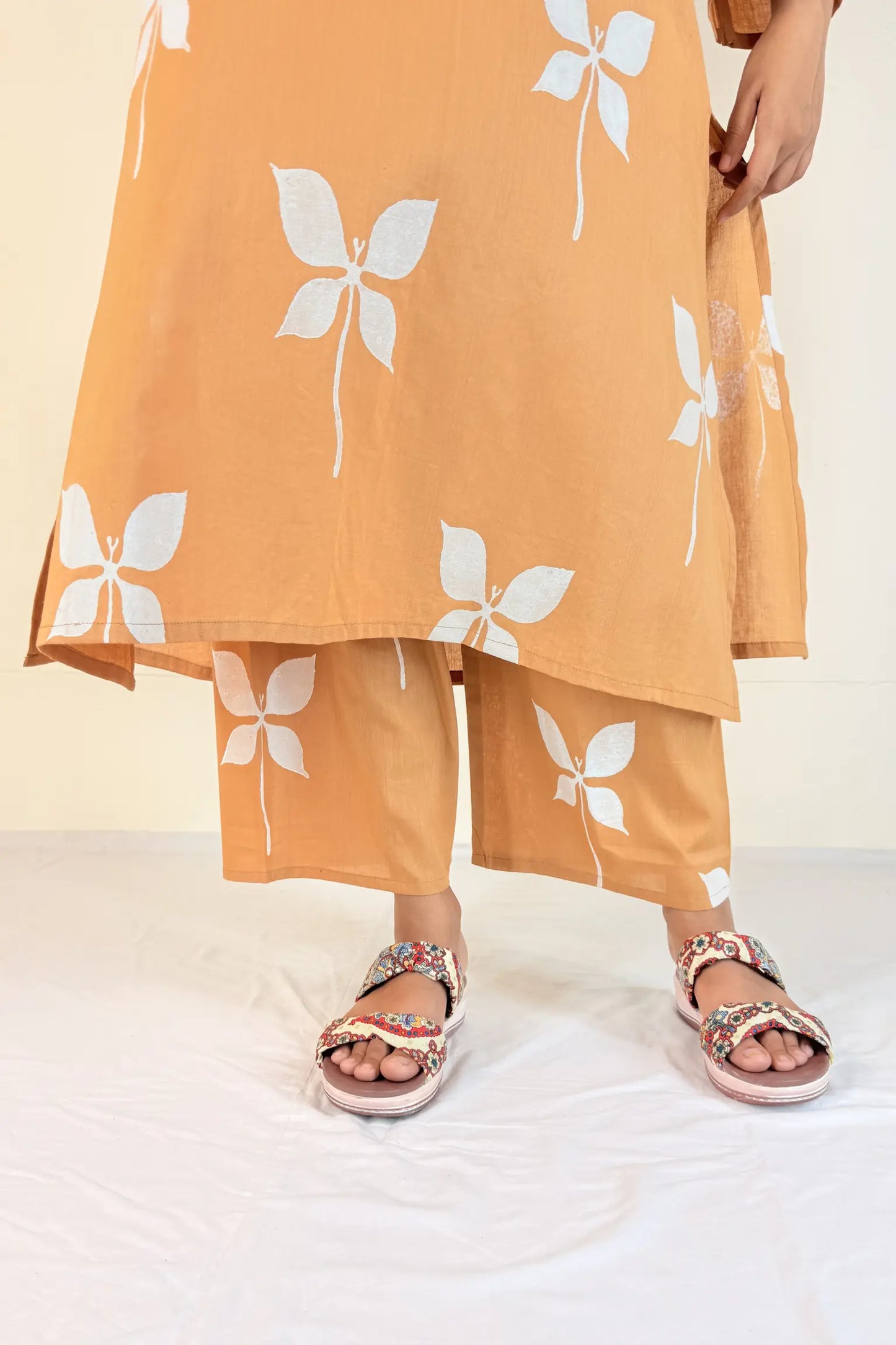 Person wearing an orange outfit with white butterfly patterns and sandals on a light background