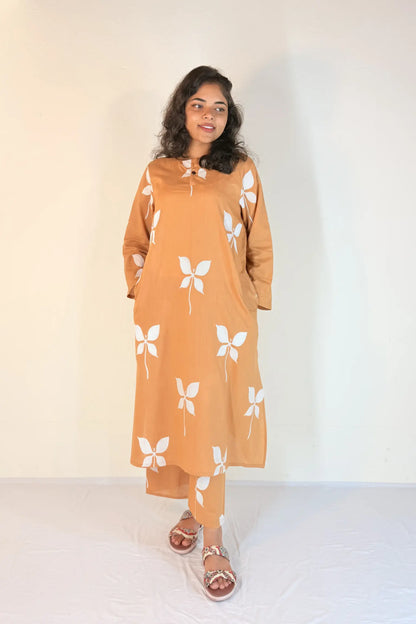 Woman wearing a mustard yellow dress with white butterfly patterns on a plain background