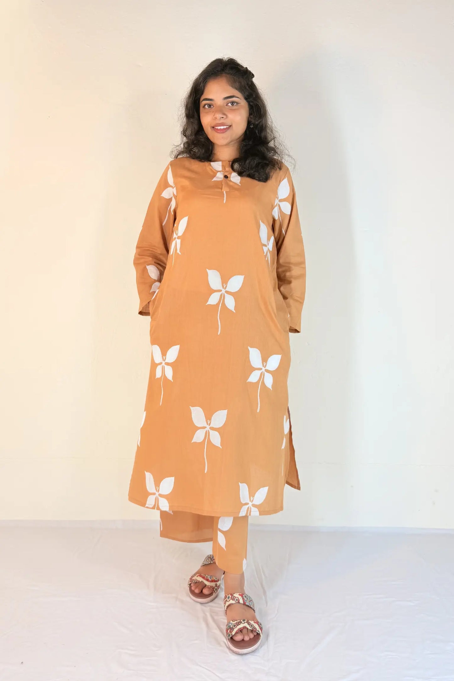 Woman wearing a mustard yellow dress with white floral patterns on a plain background