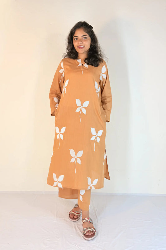 Woman wearing a mustard yellow dress with white floral patterns on a plain background