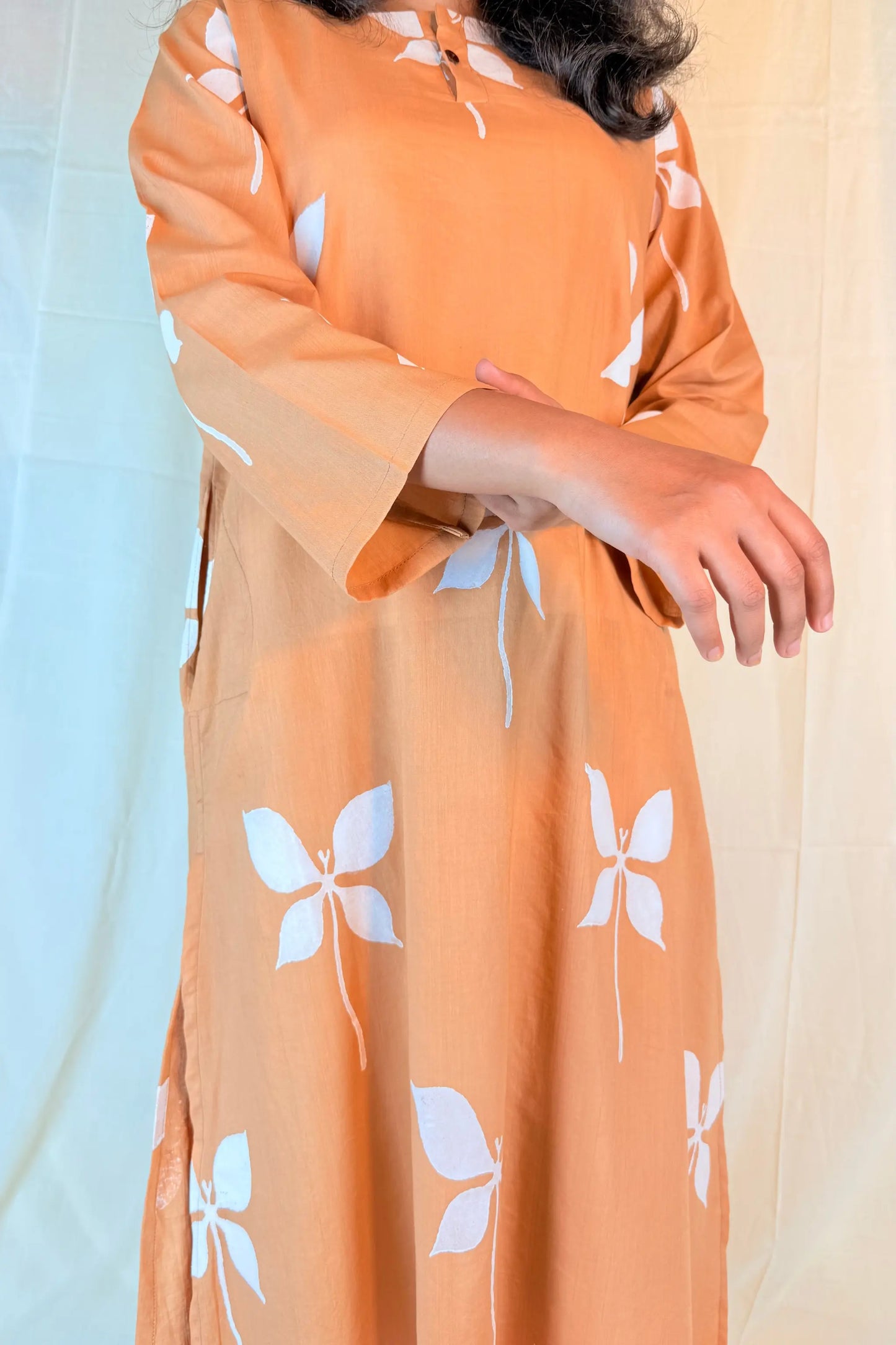 Person wearing an orange dress with white floral patterns against a light blue curtain.