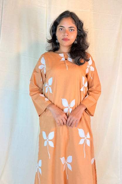 Woman wearing a peach-colored dress with white floral patterns against a plain background