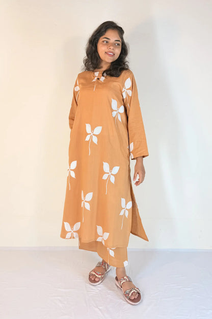 Woman wearing a long, mustard-colored dress with white floral patterns against a plain background