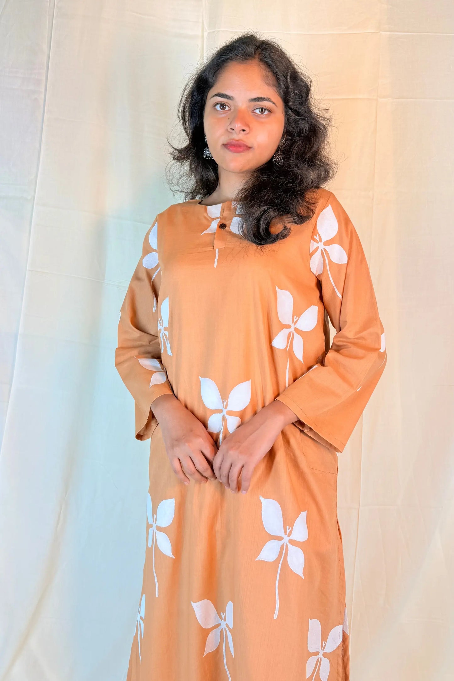 Woman wearing an orange dress with white floral patterns against a neutral background