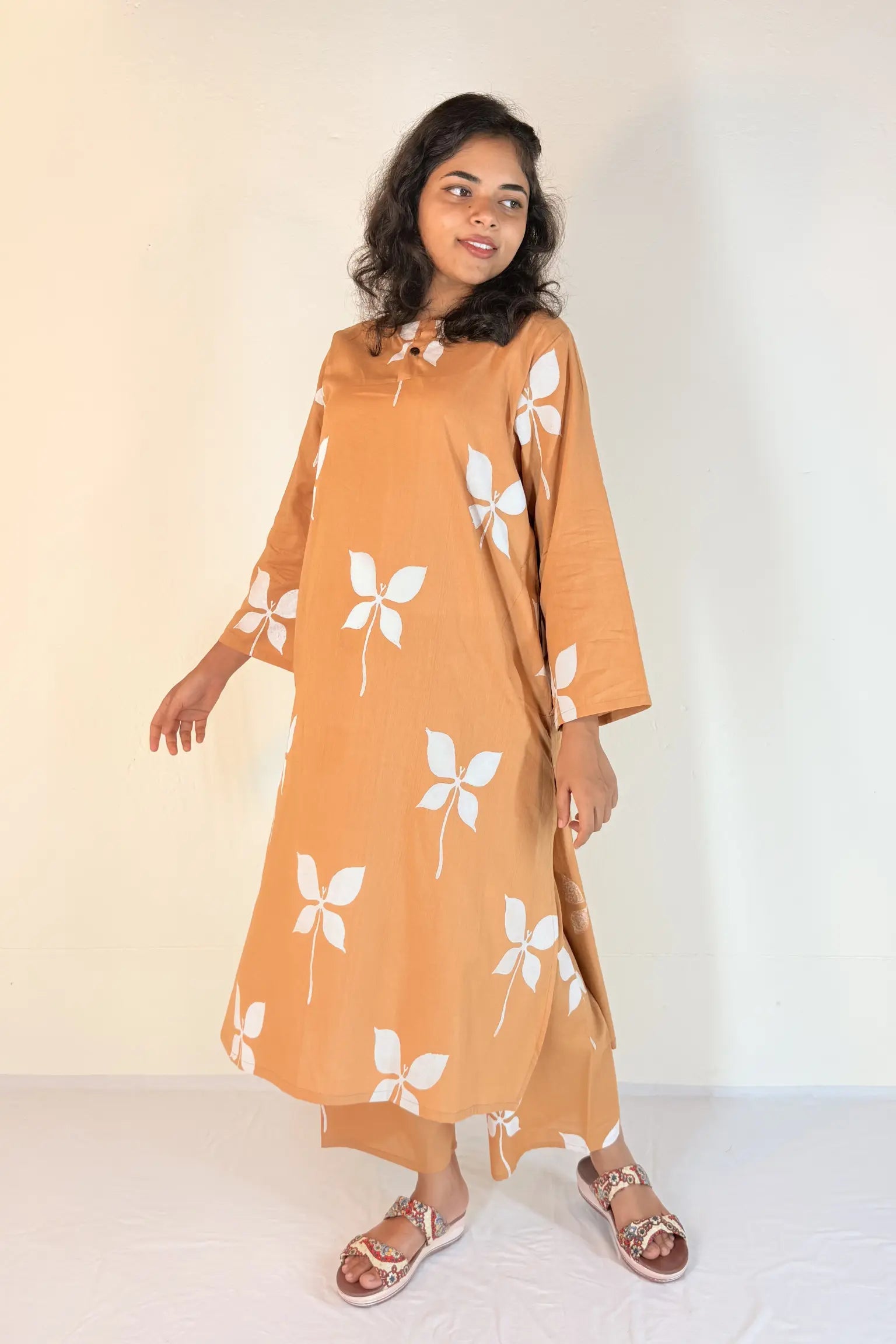 Woman wearing a mustard yellow dress with white floral patterns on a plain background