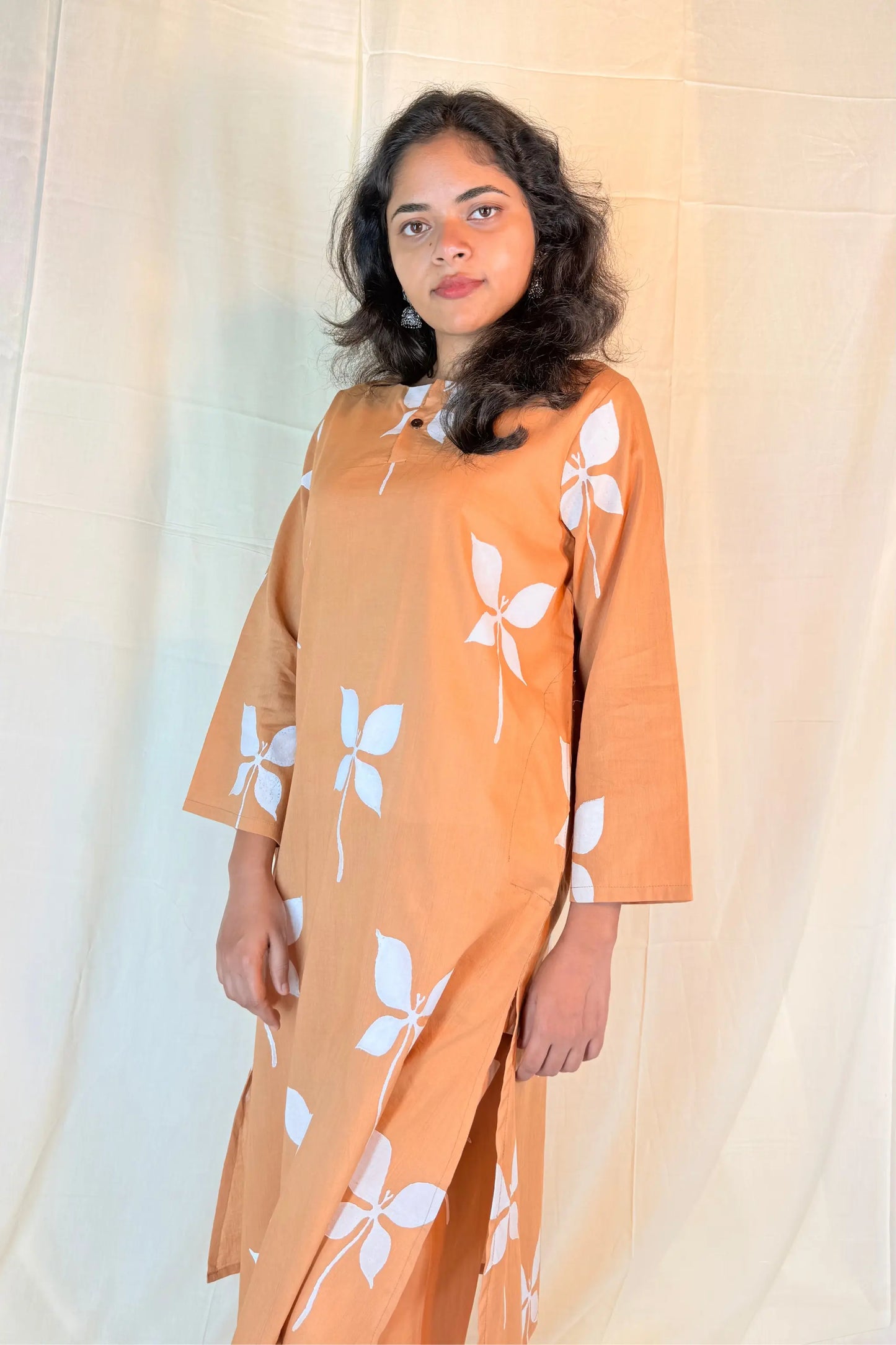 Woman wearing a brown dress with white floral patterns against a plain background